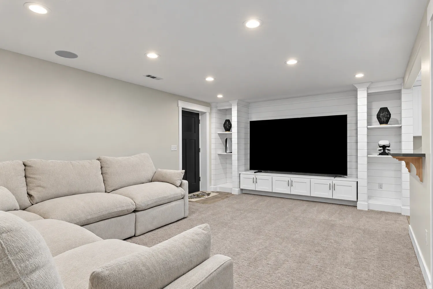 Recessed lighting, light-colored walls, dark paneled door, built-in shelving, and shiplap accent wall