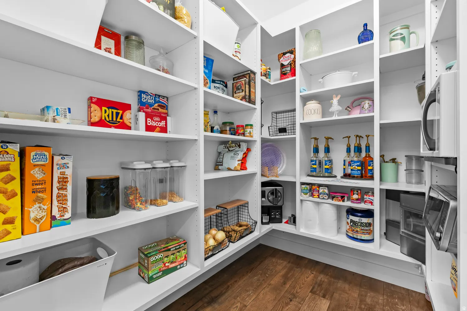 Walk-in pantry featuring white shelving, wood-finish flooring, and ample storage space