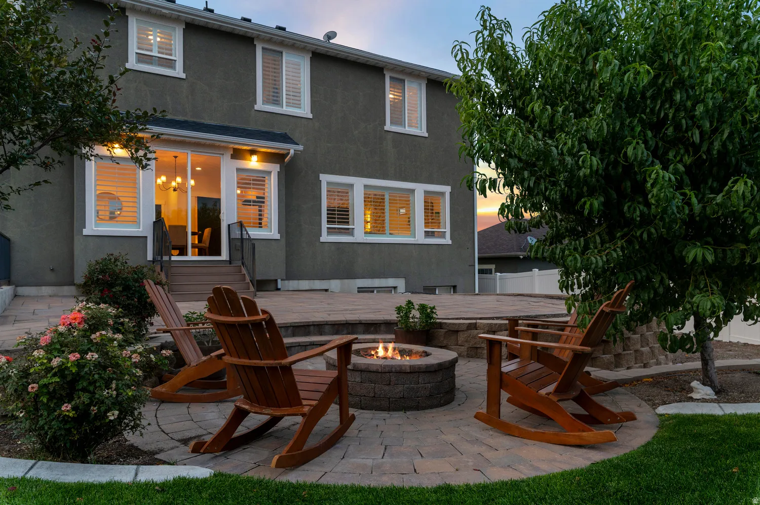 Expansive paver patio with a built-in fire pit, surrounded by mature landscaping