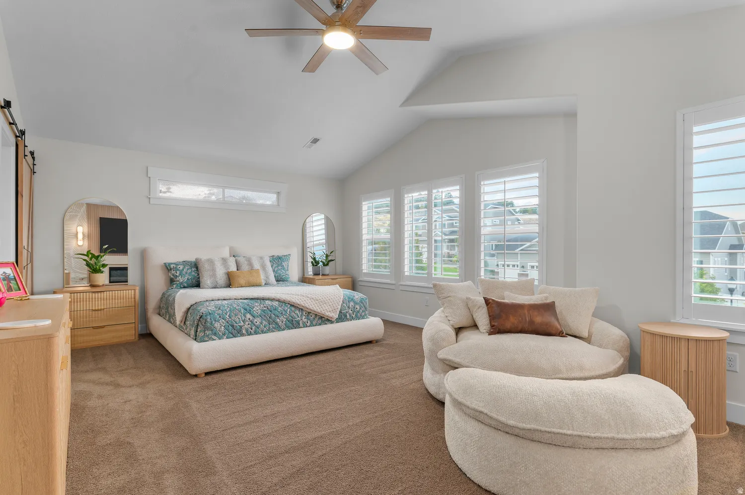 Vaulted ceiling with a wood-finish ceiling fan, multiple windows with white plantation shutters, and a sliding barn door