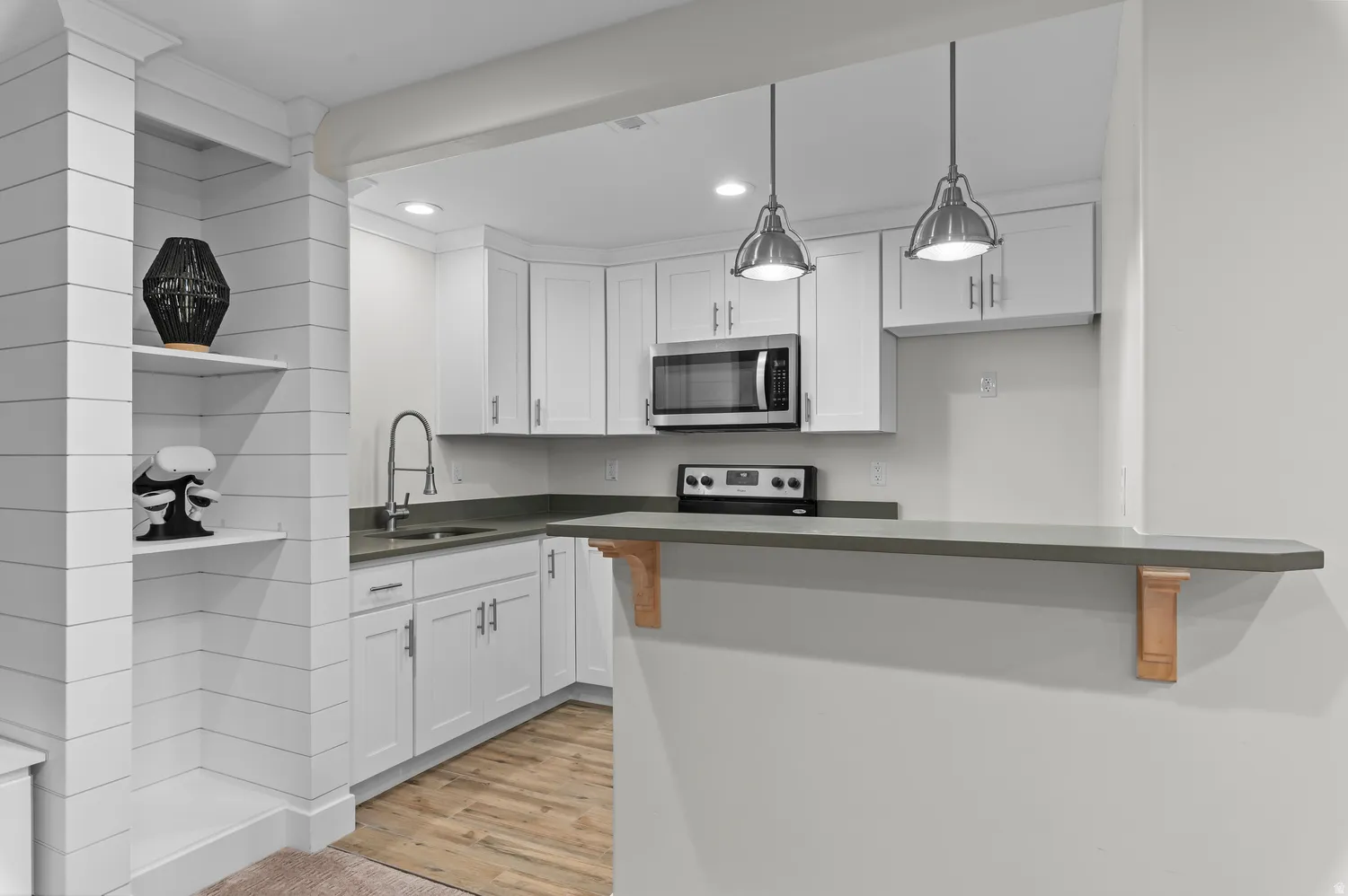 Kitchenette featuring white cabinetry, stainless steel appliances, a corner sink with a gooseneck faucet, pendant lighting, and wood-finish flooring