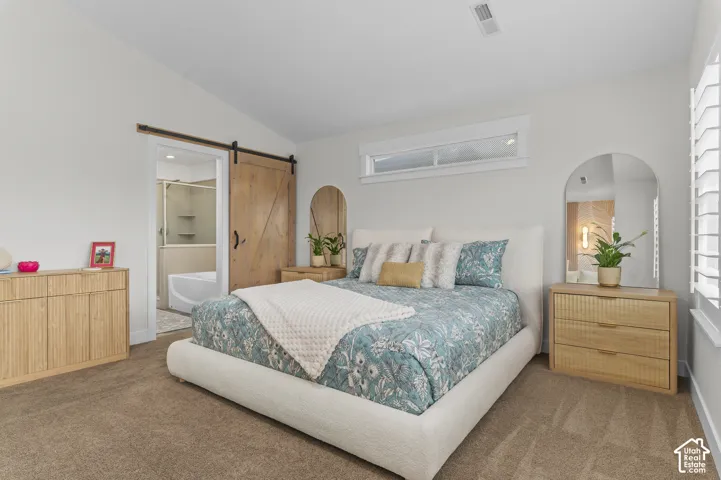 Carpeted bedroom featuring a vaulted ceiling, a wood-finish barn door, a transom window, and white plantation shutters