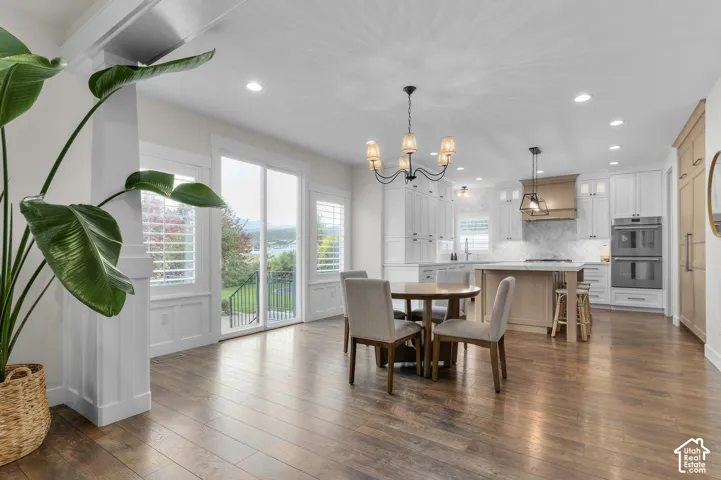 Hardwood flooring throughout, white cabinetry with integrated appliances, kitchen island with seating, pendant lighting, and sliding glass doors to exterior
