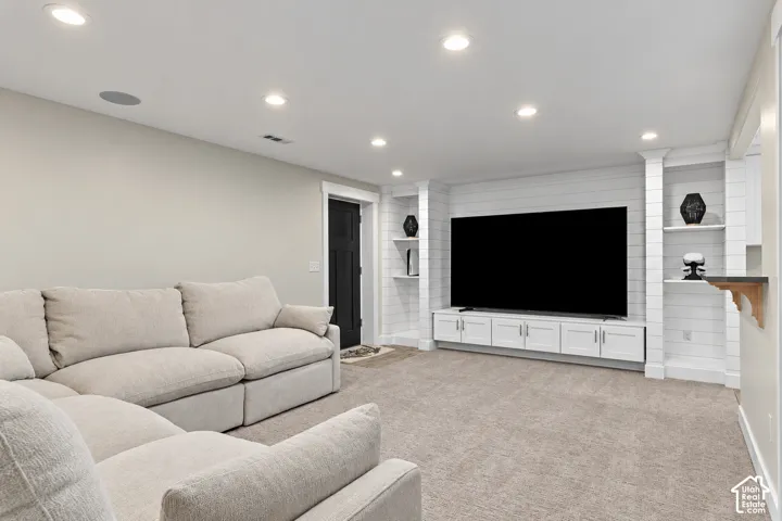 Recessed lighting, shiplap accent wall, built-in media console, built-in shelving, and light neutral carpet