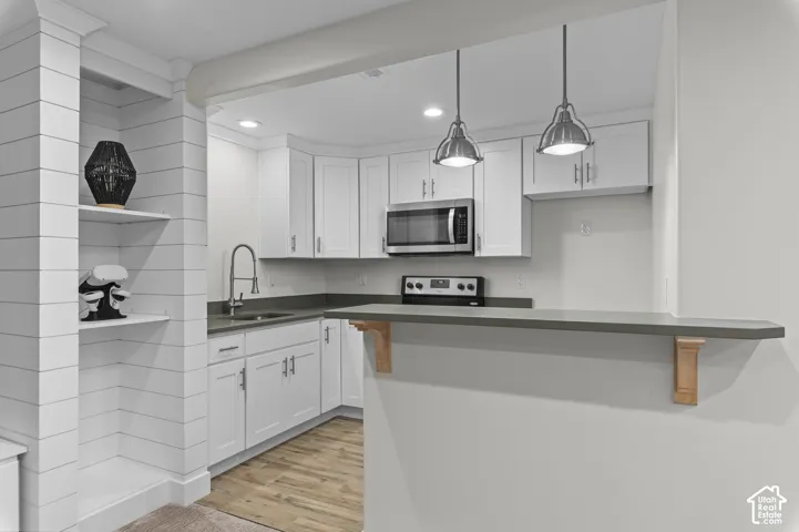 Built-in shelving, white shaker cabinetry, stainless steel appliances, dark countertop, and wood-finish flooring