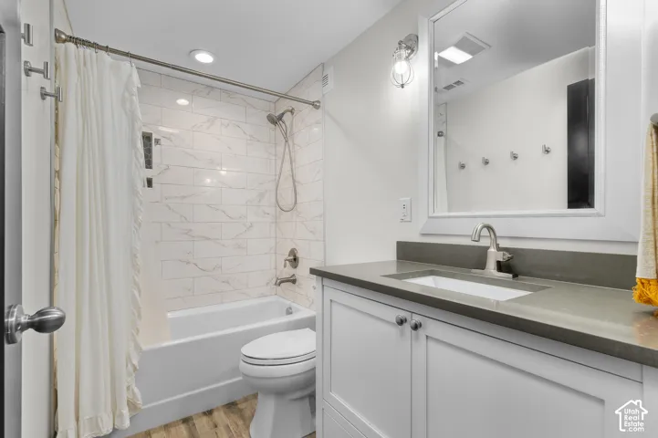 Bathroom featuring wood-finish flooring, a white vanity with shaker-style cabinetry, a gray countertop with an integrated sink, and a tiled shower-over-tub with brushed nickel fixtures