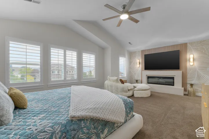 Vaulted ceiling with a ceiling fan, three windows with white plantation shutters, built-in fireplace, and integrated wall sconces