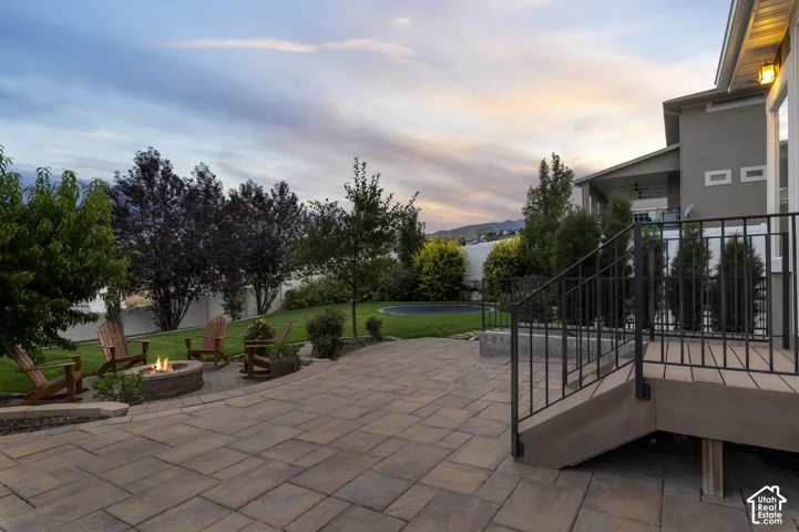 Expansive paver patio with a built-in fire pit, surrounded by a manicured lawn and mature landscaping