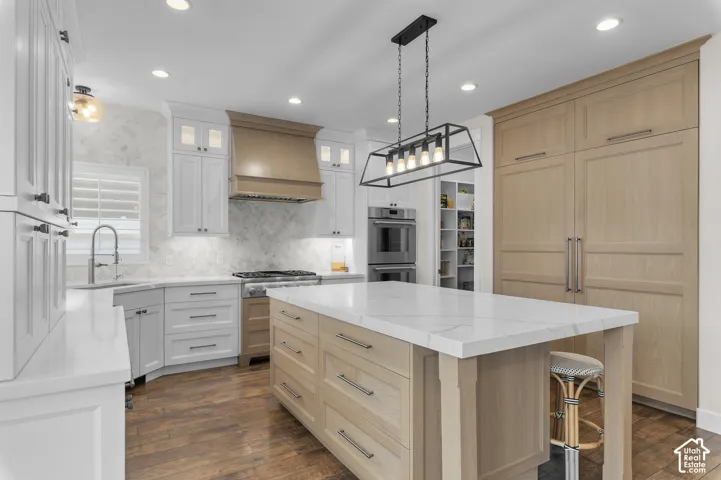 Gourmet kitchen featuring a large central island with a quartz countertop, wood-finish flooring, custom cabinetry, stainless steel appliances, and an elegant linear chandelier