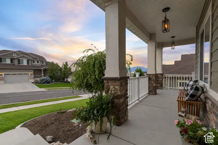 Spacious covered porch with stone-wrapped columns, white railings, and two hanging lanterns