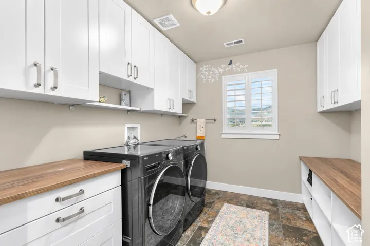 White shaker-style cabinetry, wood-finish countertops, tiled flooring, and a window with plantation shutters