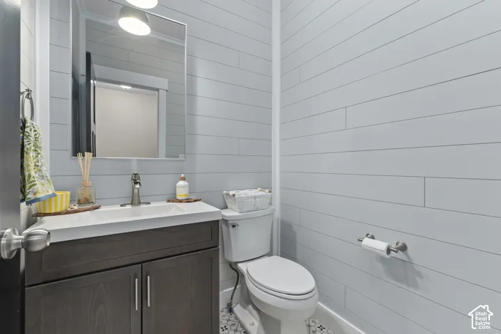 Bathroom featuring shiplap wall paneling, a dark wood-finish vanity with a single sink, an integrated countertop, and geometric-patterned floor tiling