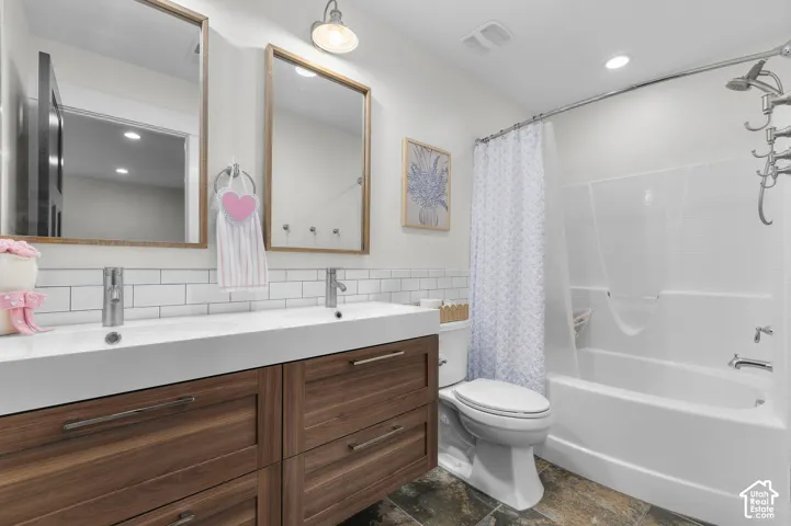 Dual vanity with wood-finish cabinetry, white subway tile backsplash, integrated dual sinks, and a built-in bathtub with shower