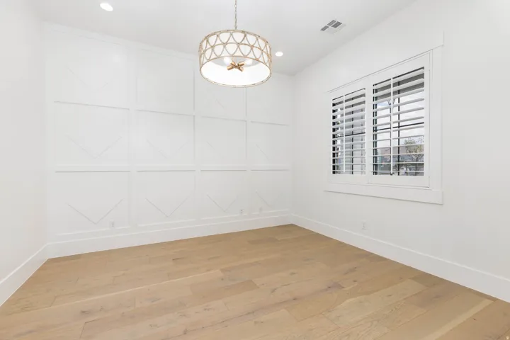 Light wood-finish flooring, accent wall with decorative paneling, and a contemporary pendant light fixture