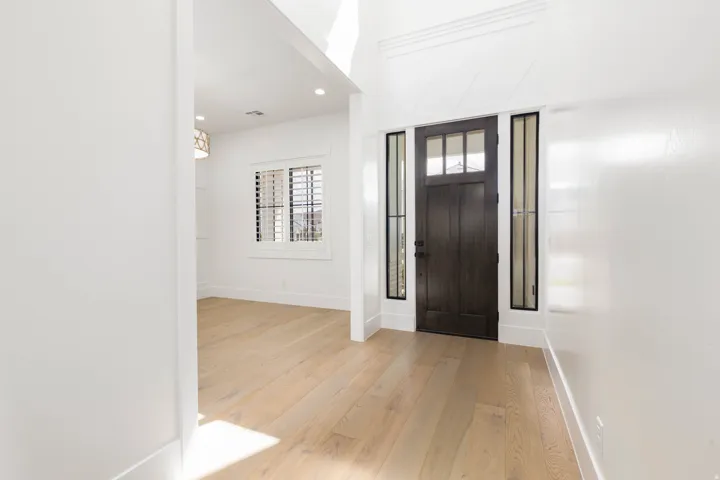 Wood-finish flooring, dark wood entry door with glass panels, side light windows, window with plantation shutters, recessed lighting