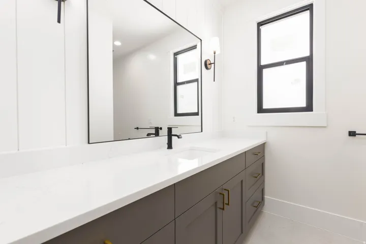 Extended vanity with an integrated sink, polished countertop, dark gray cabinetry, and brass hardware