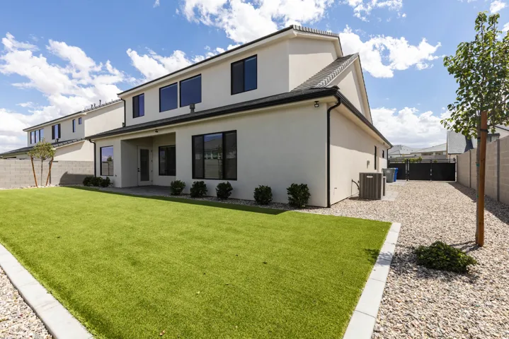 Stucco exterior with black-framed windows, artificial turf lawn, covered patio, and gravel landscaping