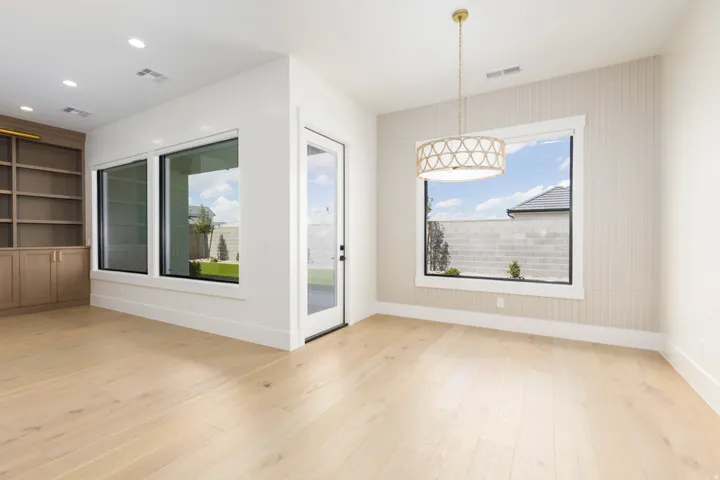 Wood-finish flooring throughout, built-in shelving with cabinetry, multiple large windows, and a glass-paneled exterior door