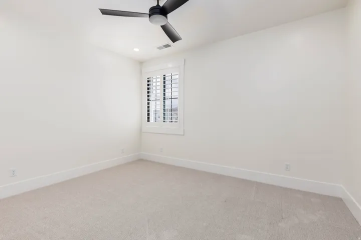 Neutral tone carpeting, white walls, and a window with white plantation shutters
