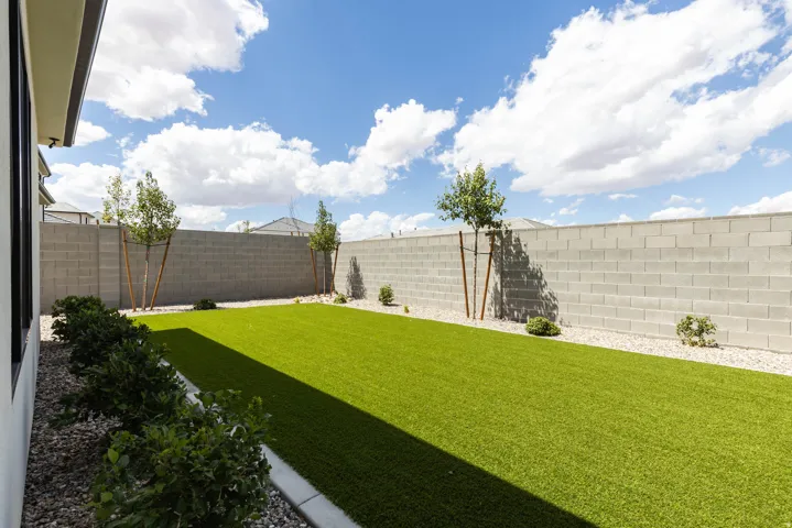 Expansive backyard featuring artificial turf, a block privacy wall, and decorative landscaping