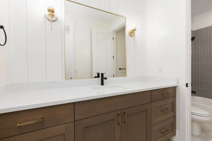 Wood-finish vanity with gold-tone hardware, white countertop, and rectangular undermount sink with a matte black faucet