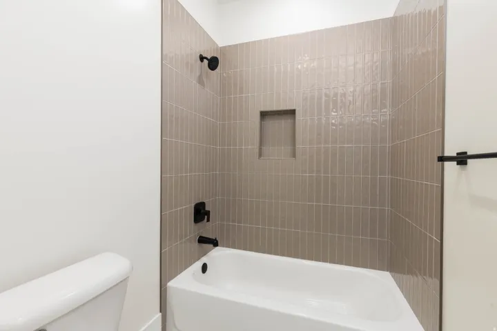 Bathtub with matte black fixtures, subway tile surround, and an integrated shower niche