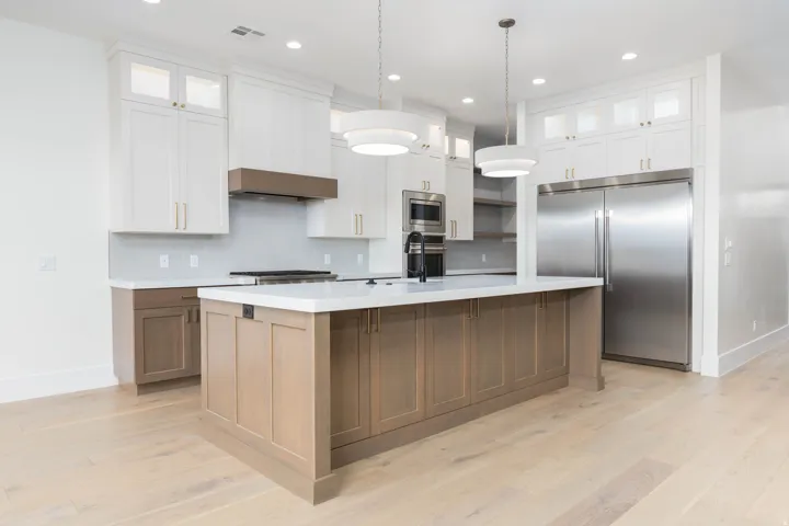 Kitchen featuring an expansive center island, integrated stainless steel refrigerator, built-in microwave, gas range, and wood-finish flooring