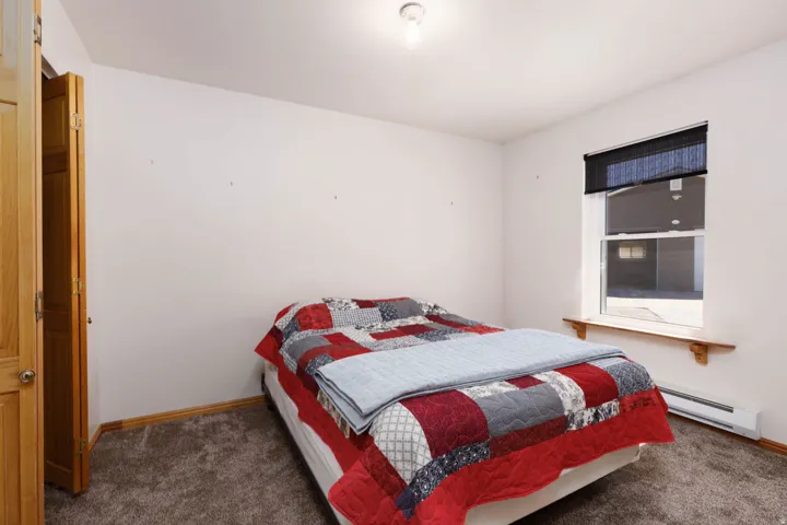 Carpeted flooring with neutral wall tones, a single window with a roller shade, and wood-finish trim