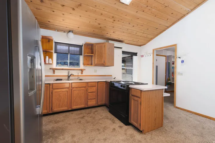 Wood-finish vaulted ceiling, stainless steel refrigerator, wood-finish cabinetry, solid surface countertops, and electric range