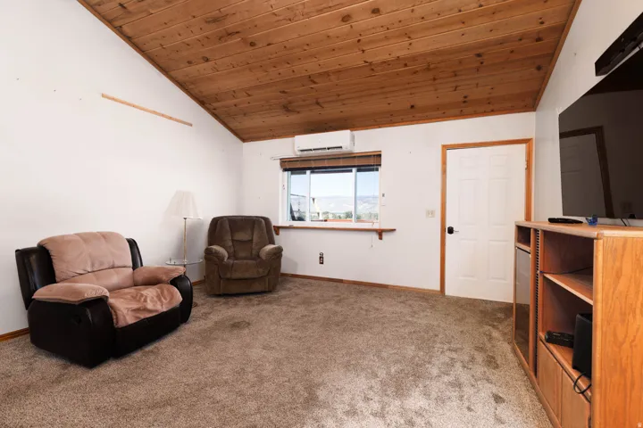 Vaulted wood-finish ceiling, mounted mini-split system, window with horizontal blinds, paneled door, and carpeted flooring