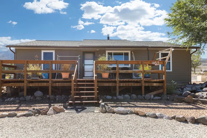 Single-story home featuring a broad wood-finish deck, exterior siding, and a gravel foreground