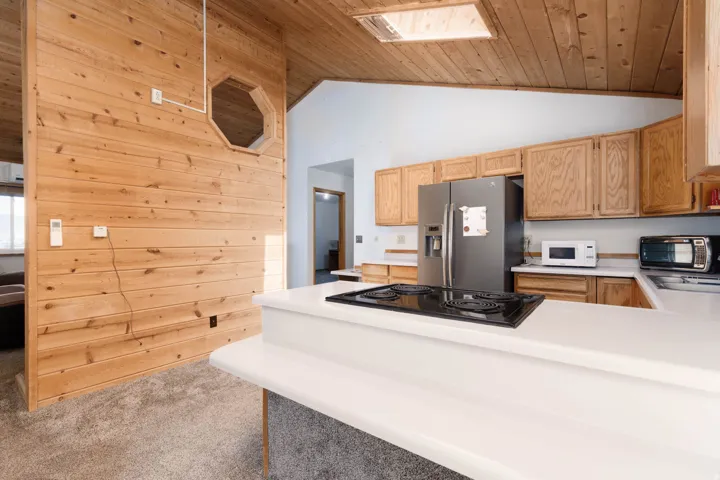 Vaulted wood-paneled ceiling with skylight, wood-paneled accent wall with decorative opening, kitchen with wood cabinetry, and white countertops