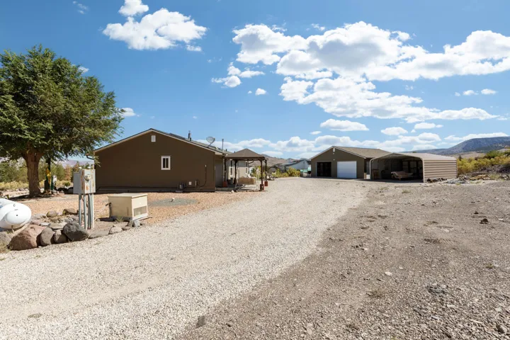 Gravel driveway leading to two structures, including a two-car garage with a roll-up door and an attached metal carport