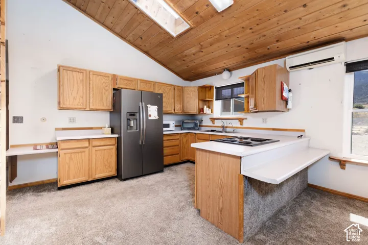 Vaulted wood-paneled ceiling with skylight, wood cabinetry, white countertops, built-in cooktop, and stainless steel refrigerator