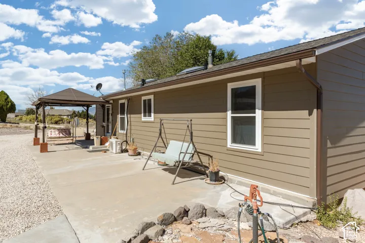 Exterior siding, concrete patio, white-framed windows, brown gutters, and a covered pergola
