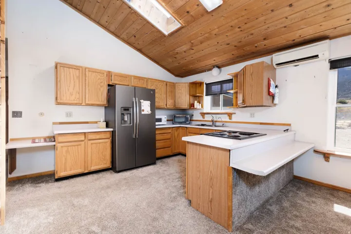 Vaulted wood-paneled ceiling with skylight, wood cabinetry, white countertops, built-in cooktop, and stainless steel refrigerator