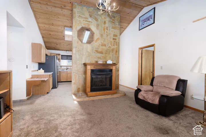 Vaulted wood-paneled ceiling, stone-clad fireplace with wood mantel, built-in shelving, wood-finish cabinetry, and stainless steel refrigerator