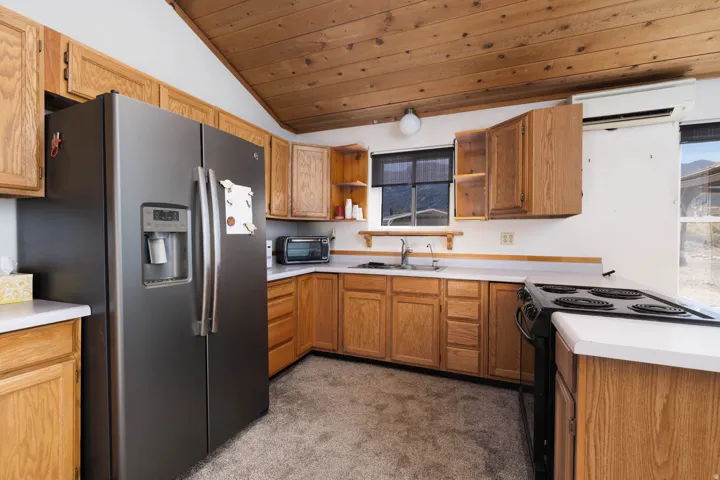 Kitchen featuring wood cabinetry, white countertops, stainless steel refrigerator, electric range, and wood-paneled ceiling