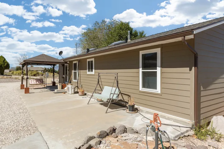 Exterior siding, concrete patio, white-framed windows, brown gutters, and a covered pergola