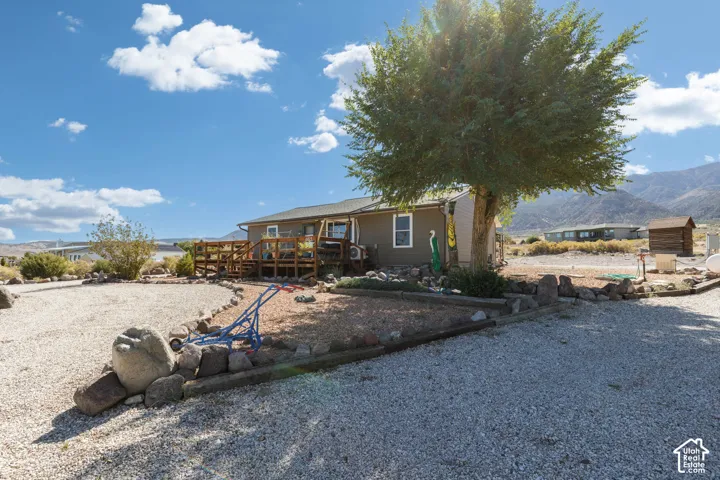 Gravel landscaping with natural rock accents, mature tree, multi-level wood deck, and mountain backdrop