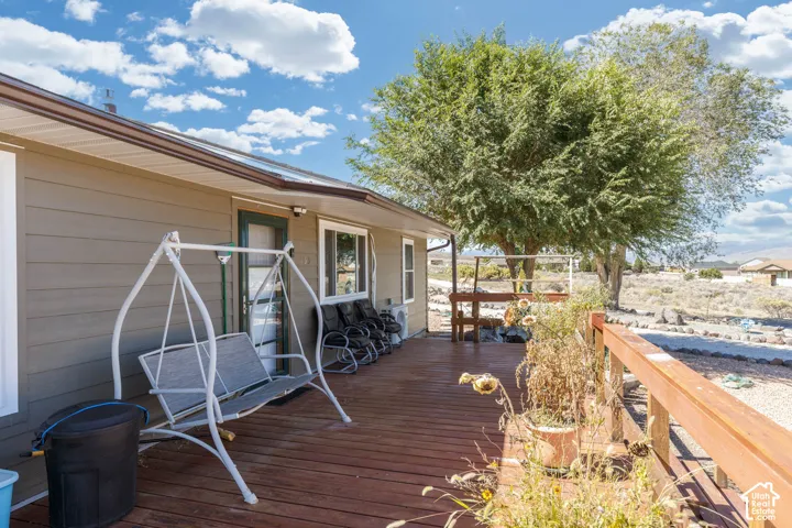 Wood-tone deck with wood railing, tan siding, and a large deciduous tree