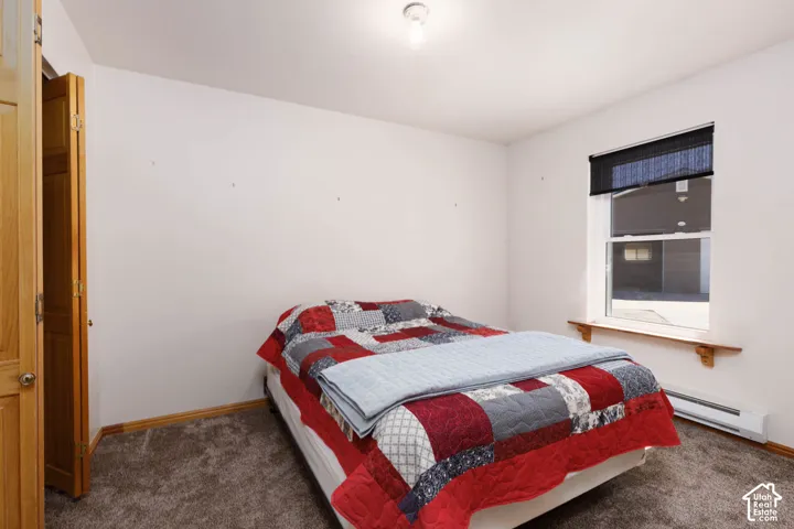 Carpeted flooring with neutral wall tones, a single window with a roller shade, and wood-finish trim