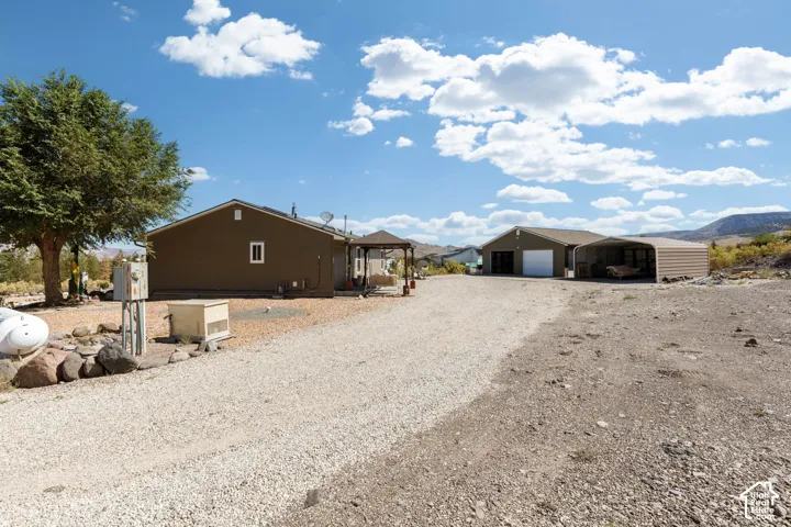 Gravel driveway leading to two structures, including a two-car garage with a roll-up door and an attached metal carport