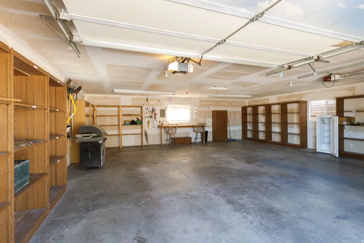 Spacious garage with concrete flooring, multiple built-in wood-finish shelving units, and a work area with a window