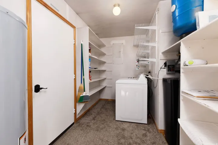 Utility area with built-in shelving, a washer, a water heater, and a water pressure tank