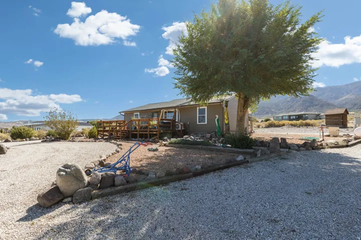 Gravel landscaping with natural rock accents, mature tree, multi-level wood deck, and mountain backdrop