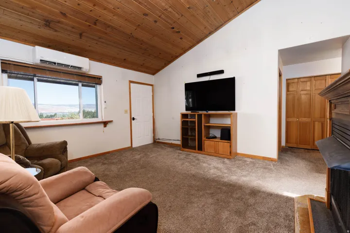 Vaulted wood-paneled ceiling, large window, built-in air conditioning unit, and wood-finish bi-fold closet doors