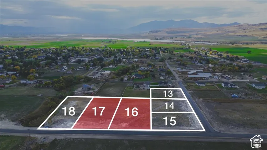 Aerial view of undeveloped land parcels featuring paved road access, clear boundary demarcations, and mountain range backdrop