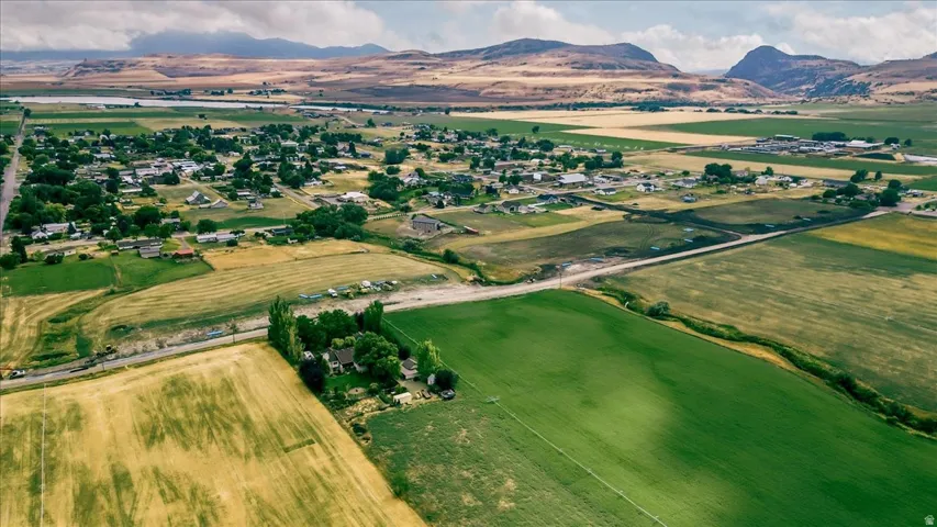 Expansive rural landscape featuring a mix of green and golden fields, distant mountains, and a community of homes