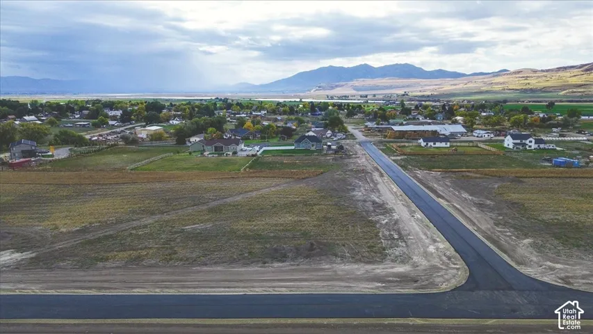 Aerial perspective of expansive residential acreage featuring paved street access, open land, and prominent mountain backdrops